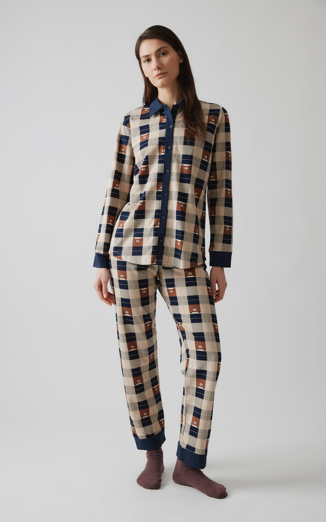 Γυναικείο μοντέλο με μακριά καστανά μαλλιά ποζάρει όρθιο σε φυσική στάση, φορώντας καρό πιτζάμα με μπεζ, μπλε και καφέ αποχρώσεις και μοτίβα αρκουδάκια.