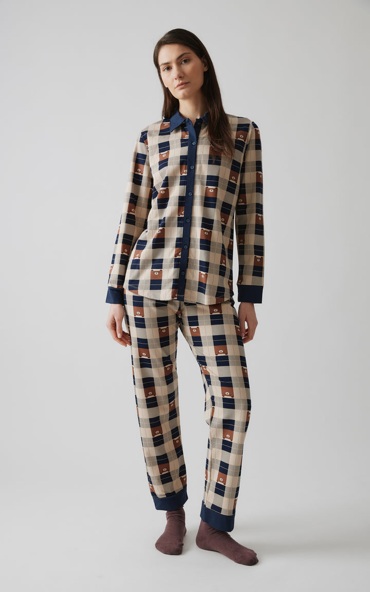 Γυναικείο μοντέλο με μακριά καστανά μαλλιά ποζάρει όρθιο σε φυσική στάση, φορώντας καρό πιτζάμα με μπεζ, μπλε και καφέ αποχρώσεις και μοτίβα αρκουδάκια.