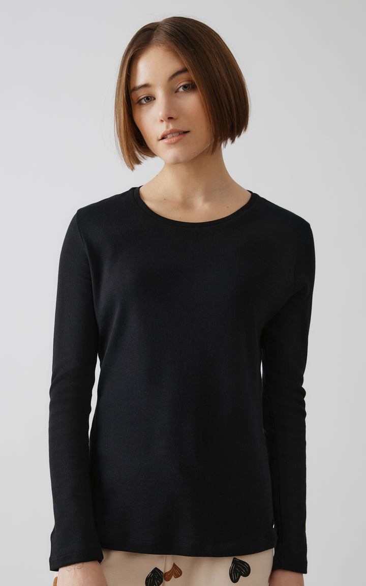 Γυναίκα με κοντό καρέ φορά μαύρη μπλούζα πιτζάμας με μακριά μανίκια και μπεζ παντελόνι με μαύρες και καφέ καρδιές.