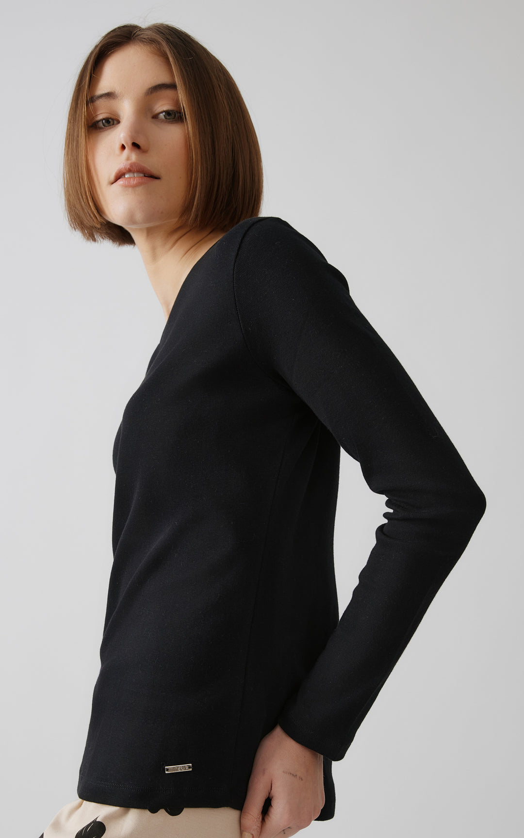 Προφίλ γυναίκας που φορά μαύρη μακρυμάνικη μπλούζα πιτζάμας με απλό σχέδιο, σε μίνιμαλ φόντο.