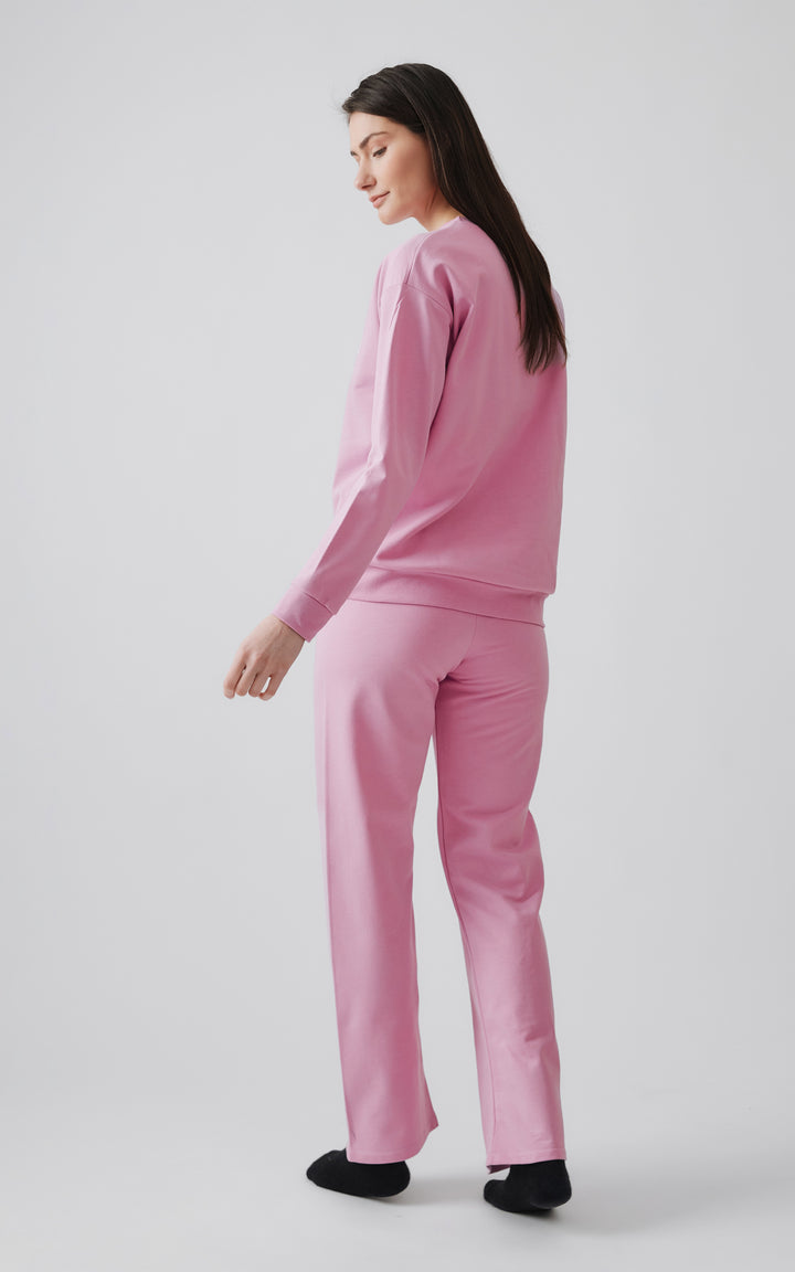 Μοντέλο με μακριά μαλλιά φοράει ροζ χειμερινές πιτζάμες και μαύρες κάλτσες μπροστά από γκρι φόντο. 