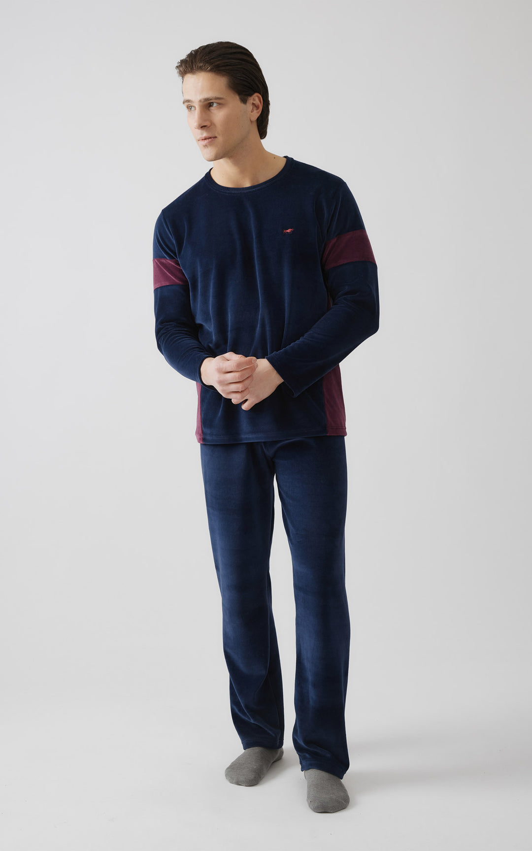 Άντρας ποζάρει φορώντας μπλε βελουτέ ανδρική πιτζάμα με μακρύ μανίκι και μπορντό λεπτομέρειες στα χέρια και στα πλάγια.
