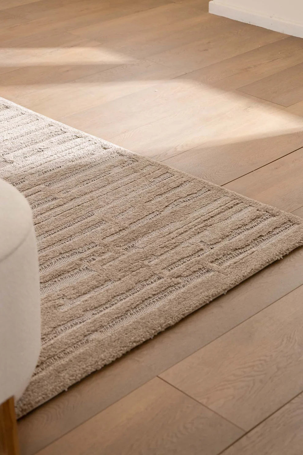 Λεπτομέρεια γωνίας του μοντέρνου χαλιού Chiara Royal Carpet σε καφέ απόχρωση με ανάγλυφη υφή και γραμμικά μοτίβα, στρωμένο σε ανοιχτό ξύλινο δάπεδο με φυσικό φωτισμό.