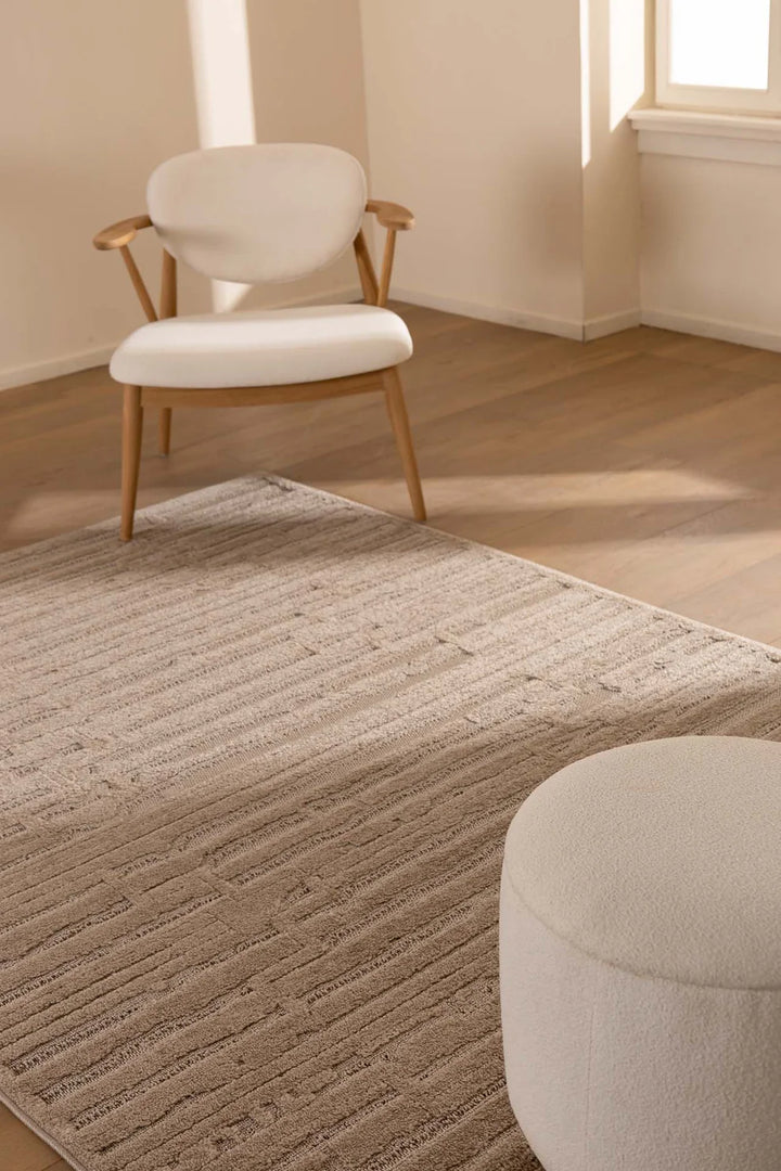 Μοντέρνο χαλί Chiara Royal Carpet σε καφέ απόχρωση με ανάγλυφη υφή και γραμμικά μοτίβα, τοποθετημένο σε ξύλινο δάπεδο minimal σαλονιού με φυσικό φωτισμό και ουδέτερα έπιπλα.