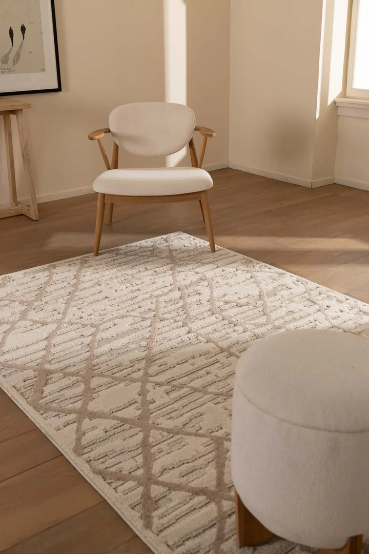 Μοντέρνο χαλί Chiara Royal Carpet σε μπεζ και εκρού αποχρώσεις με ανάγλυφο γεωμετρικό σχέδιο ρόμβων, τοποθετημένο σε ξύλινο δάπεδο minimal σαλονιού με φυσικό φωτισμό και ουδέτερα έπιπλα.