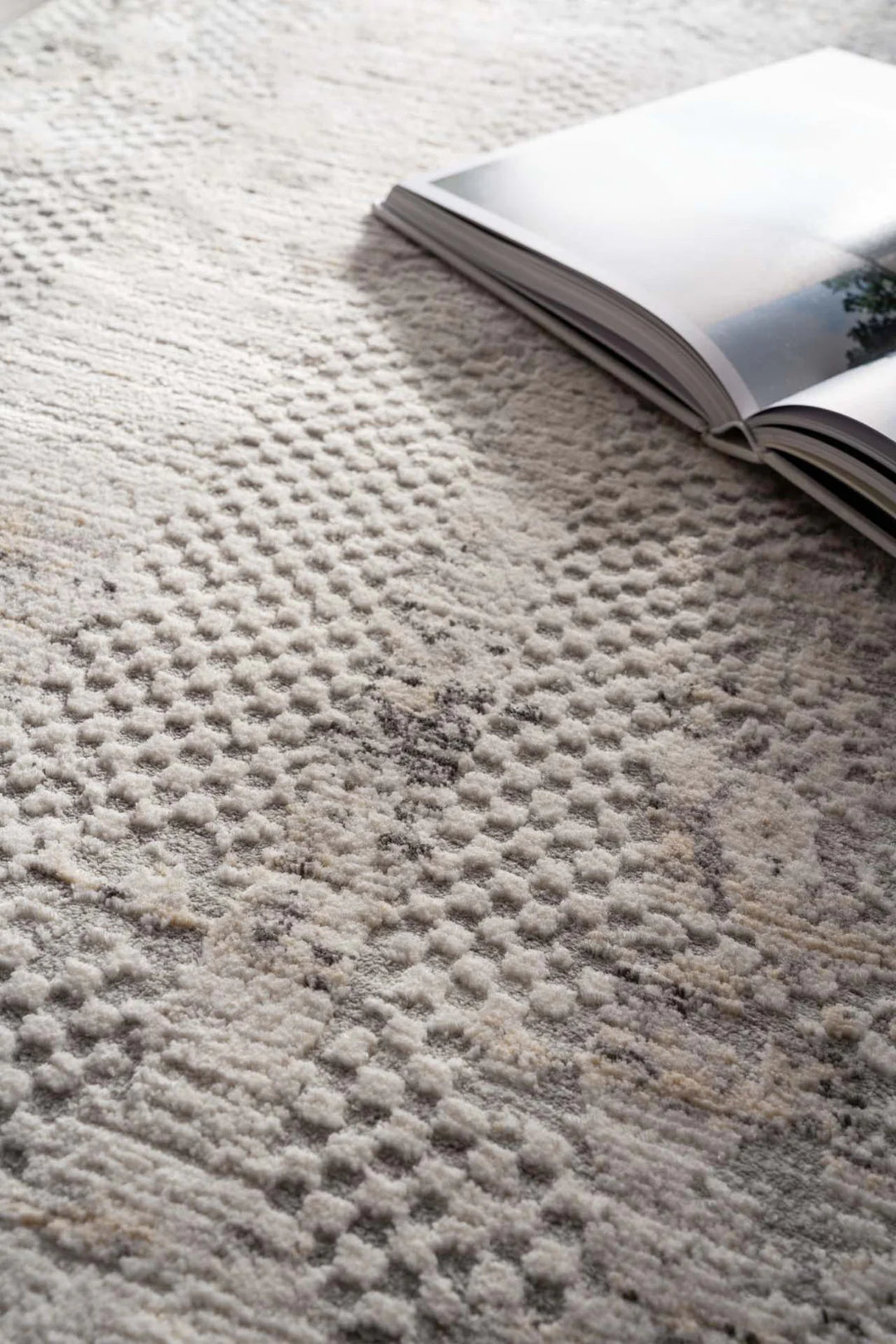 Ανάγλυφο χαλί Royal Carpet σε μπεζ, εκρού και γκρι τόνους με ανοιχτό βιβλίο επάνω σε φωτεινό χώρο.