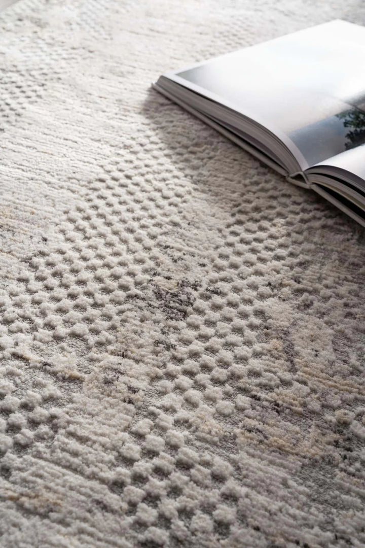 Ανάγλυφο χαλί Royal Carpet σε μπεζ, εκρού και γκρι τόνους με ανοιχτό βιβλίο επάνω σε φωτεινό χώρο.