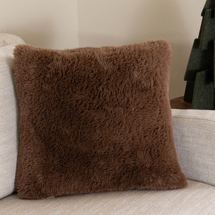Καφέ γούνινη διακοσμητική μαξιλαροθήκη Comfy Royal Carpet με απαλό μακρύ τρίχωμα, πάνω σε εκρού καναπέ.